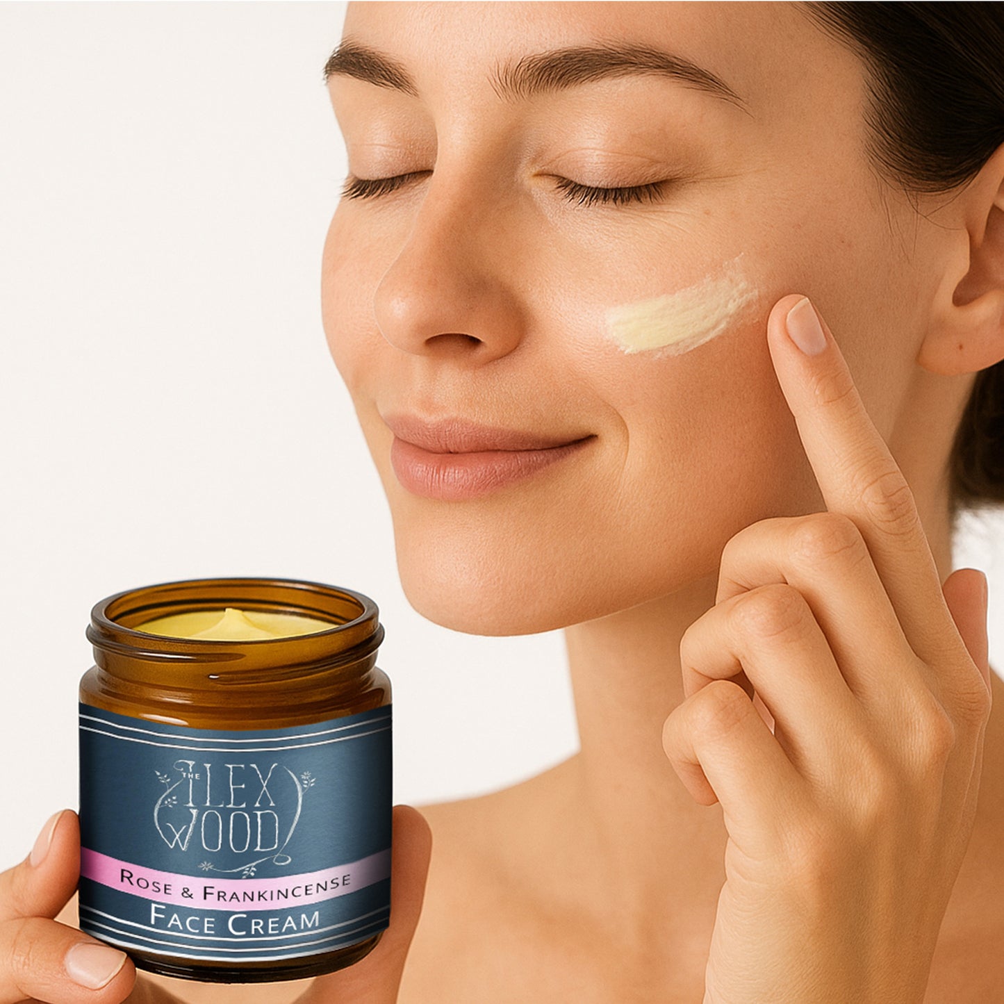 Woman applying face cream to her cheek with a jar of The Ilex Wood Rose & Frankincense Face Cream.