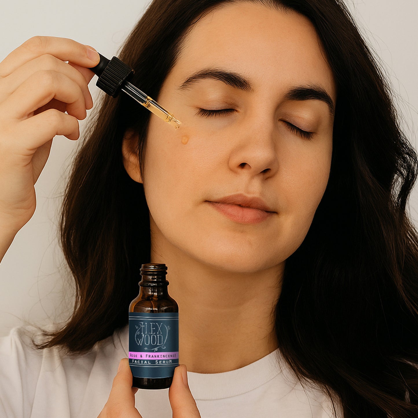 Woman applying a dropper of serum to her face with a bottle labeled The Ilex Wood Rose and Frankincense Facial Serum