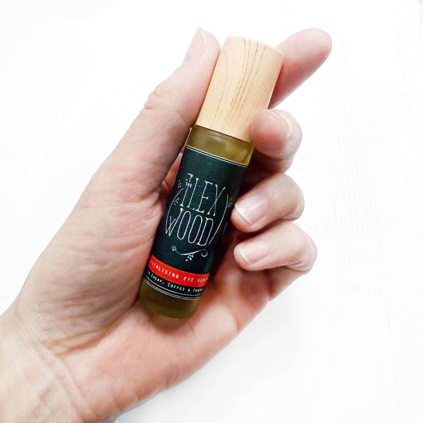 Hand holding a 10ml glass roller bottle of The Ilex Wood Revitalising Eye Serum with wooden cap