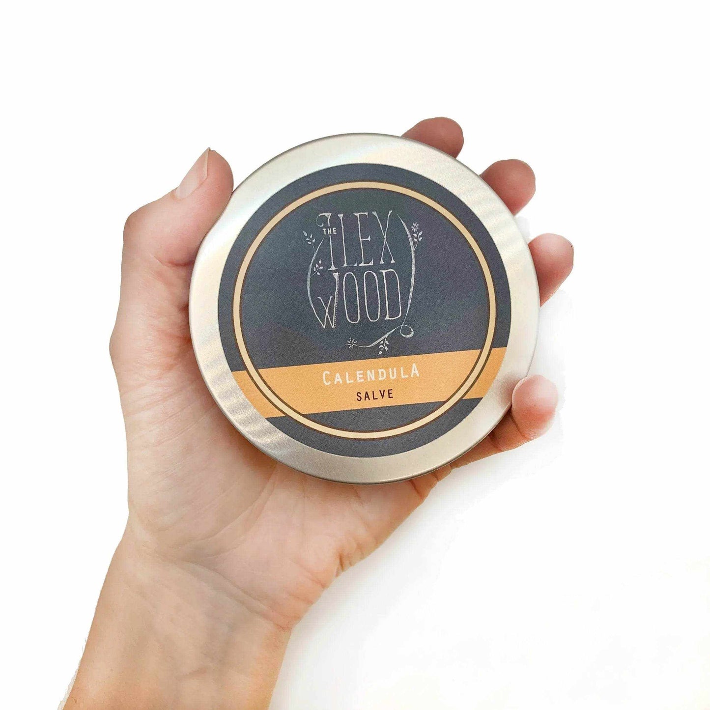 Hand holding 100ml tin of The Ilex Wood Calendula Salve natural healing skin balm