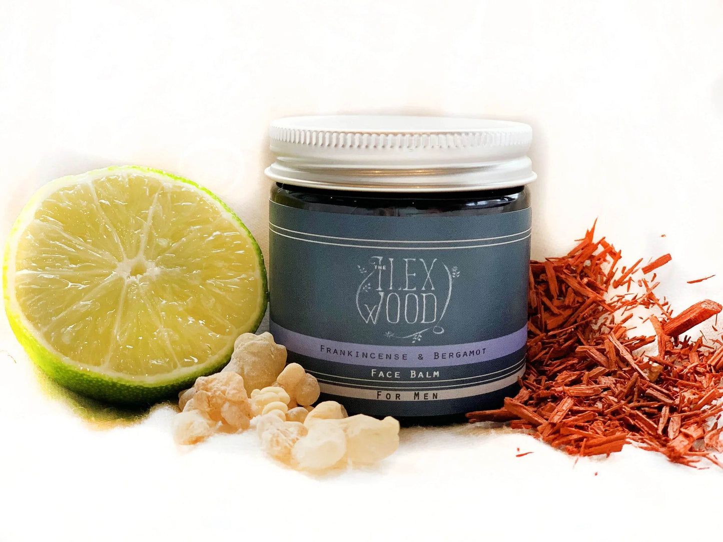 Frankincense and Bergamot Face Cream jar with lime, frankincense resin, and dried wood shavings on white background