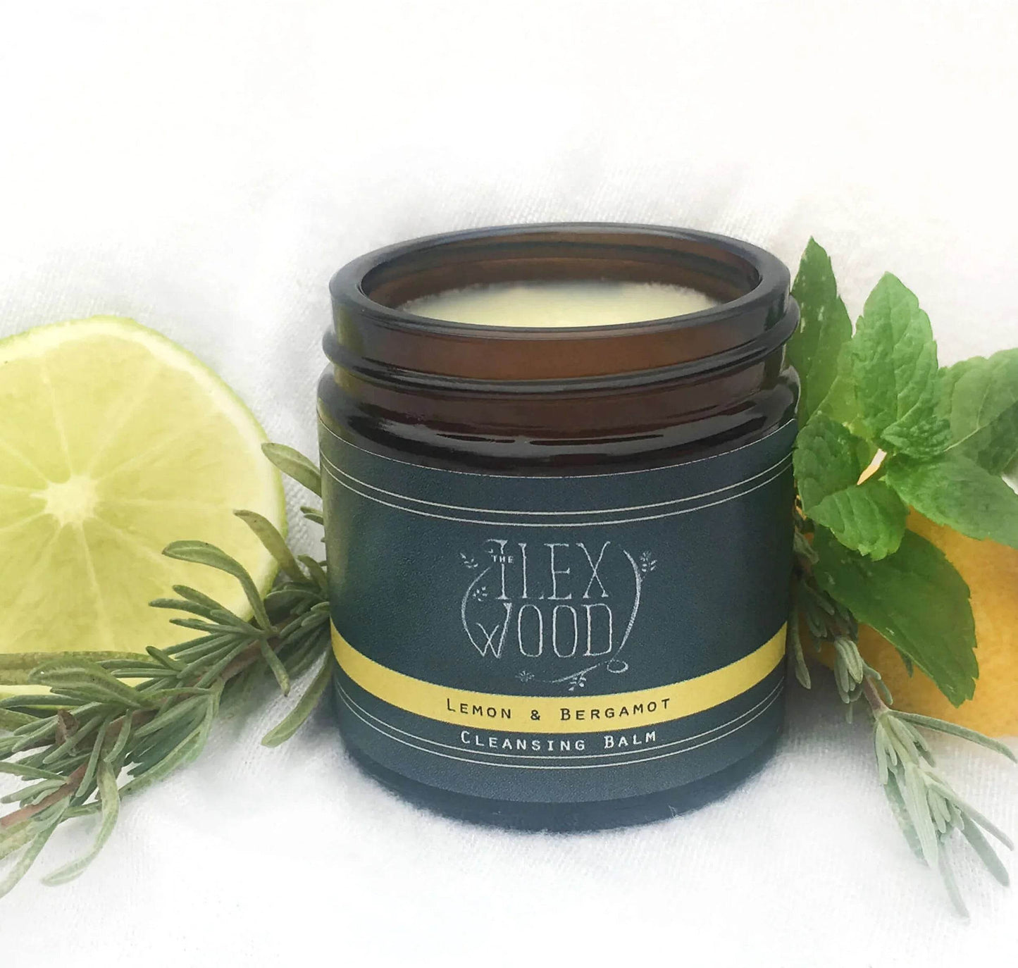 Lemon and Bergamot cleansing balm jar with fresh lemon slice and green herbs on white background